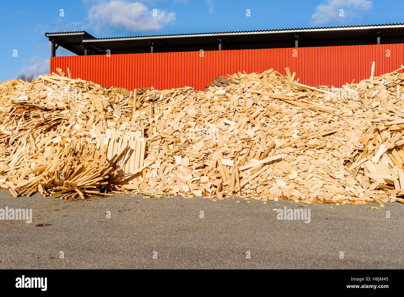 Hölzerne Trümmerhaufen vor roten Industriegebäude. Das Holz ist Abfall aus dem Sägewerk und zu Hackschnitzel erfolgt eine Stockfoto