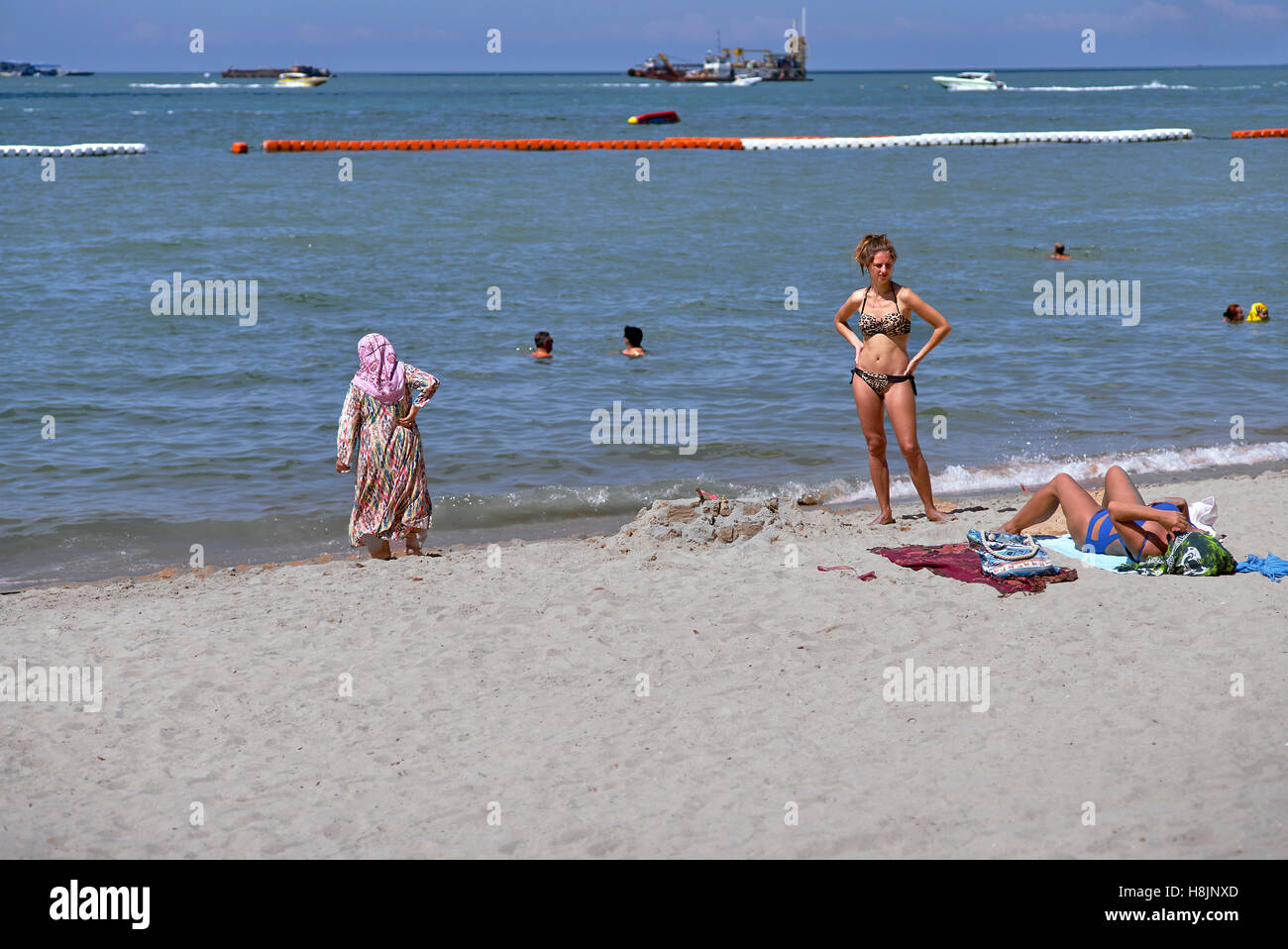 Kulturelle Konflikte. Kulturunterschied am Strand Tragen Sie Kleidung einer befreiten Westerin und ihrem mittelöstlichen Gegenstück Stockfoto