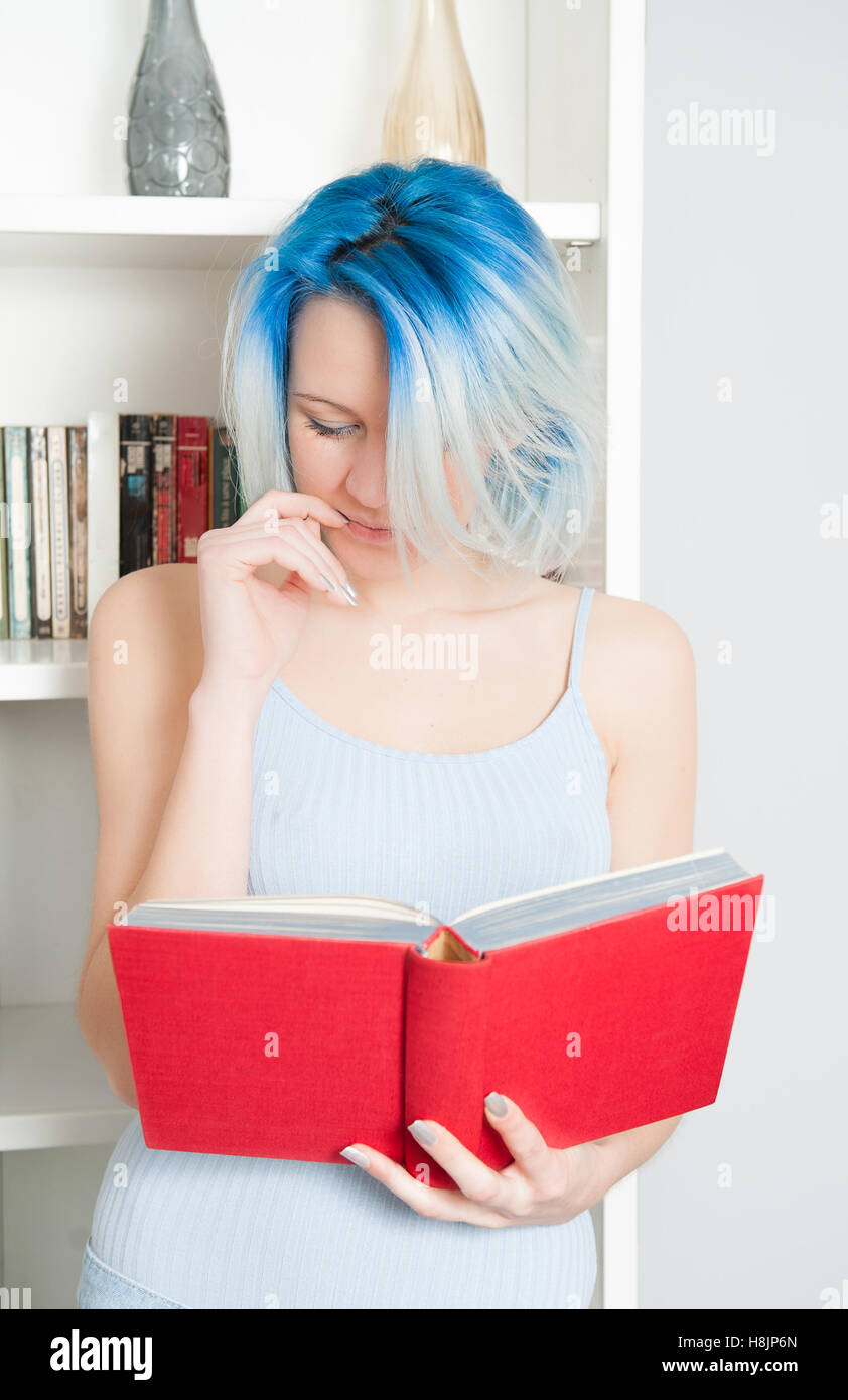 Junge hübsche Teen Frau Buch rote Abdeckung zu Hause mit weißen Bibliothek im Hintergrund Stockfoto