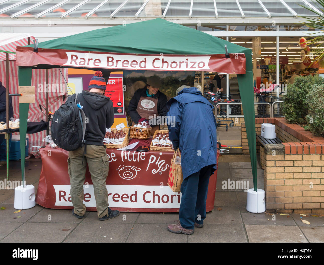Eine Frau Stall Inhaber in einem UK Bauernmarkt dienen Three Little Pigs Marke seltene Rasse Chorizo spanische Stil Würstchen Stockfoto
