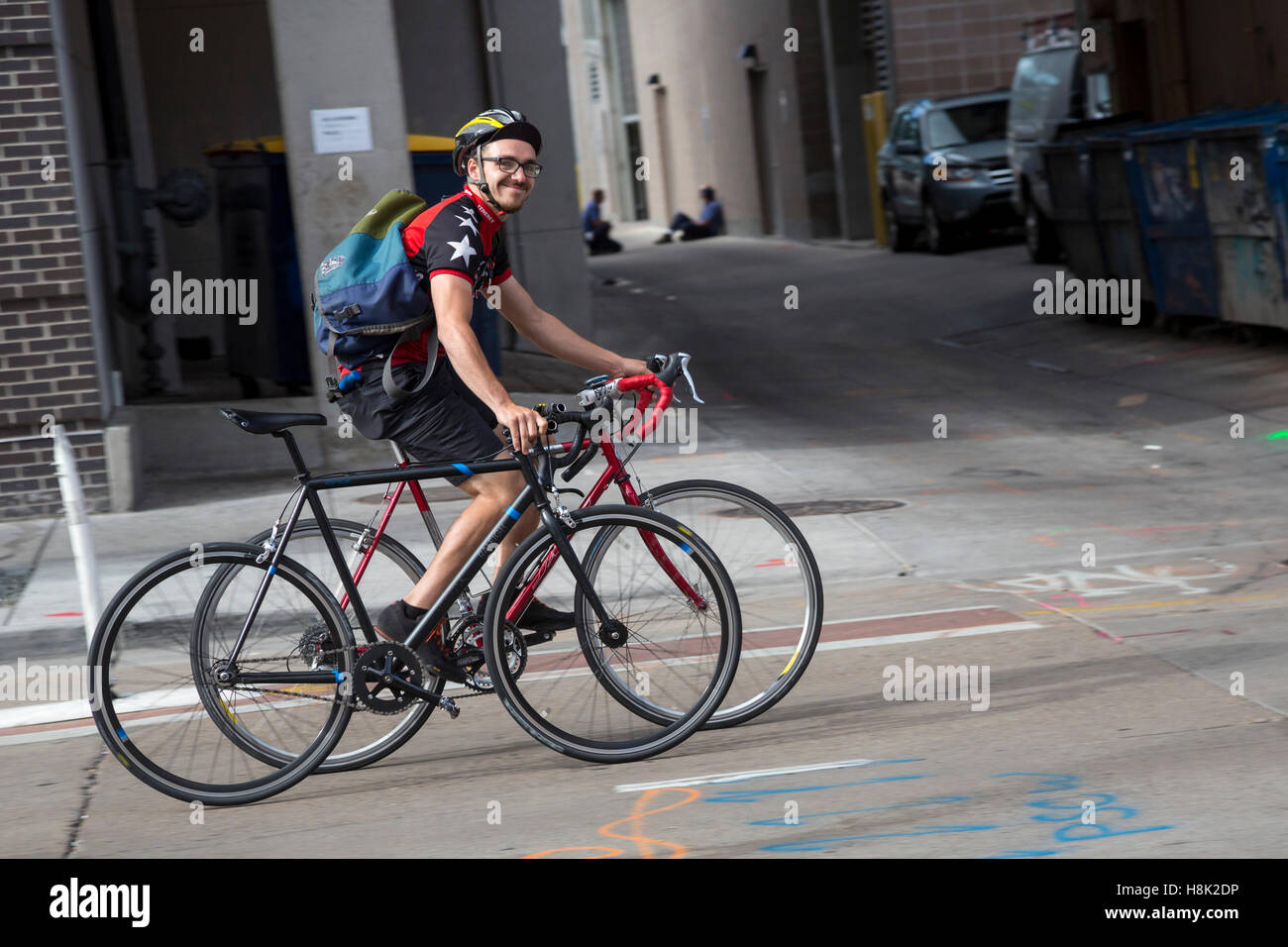 Denver, Colorado - ein junger Mann fährt zwei Fahrräder auf eine Innenstadt Straße. Stockfoto