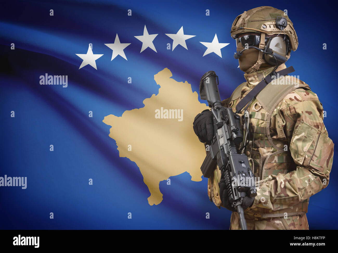 Soldat im Helm holding Maschinengewehr mit Nationalflagge auf Hintergrund - Kosovo Stockfoto