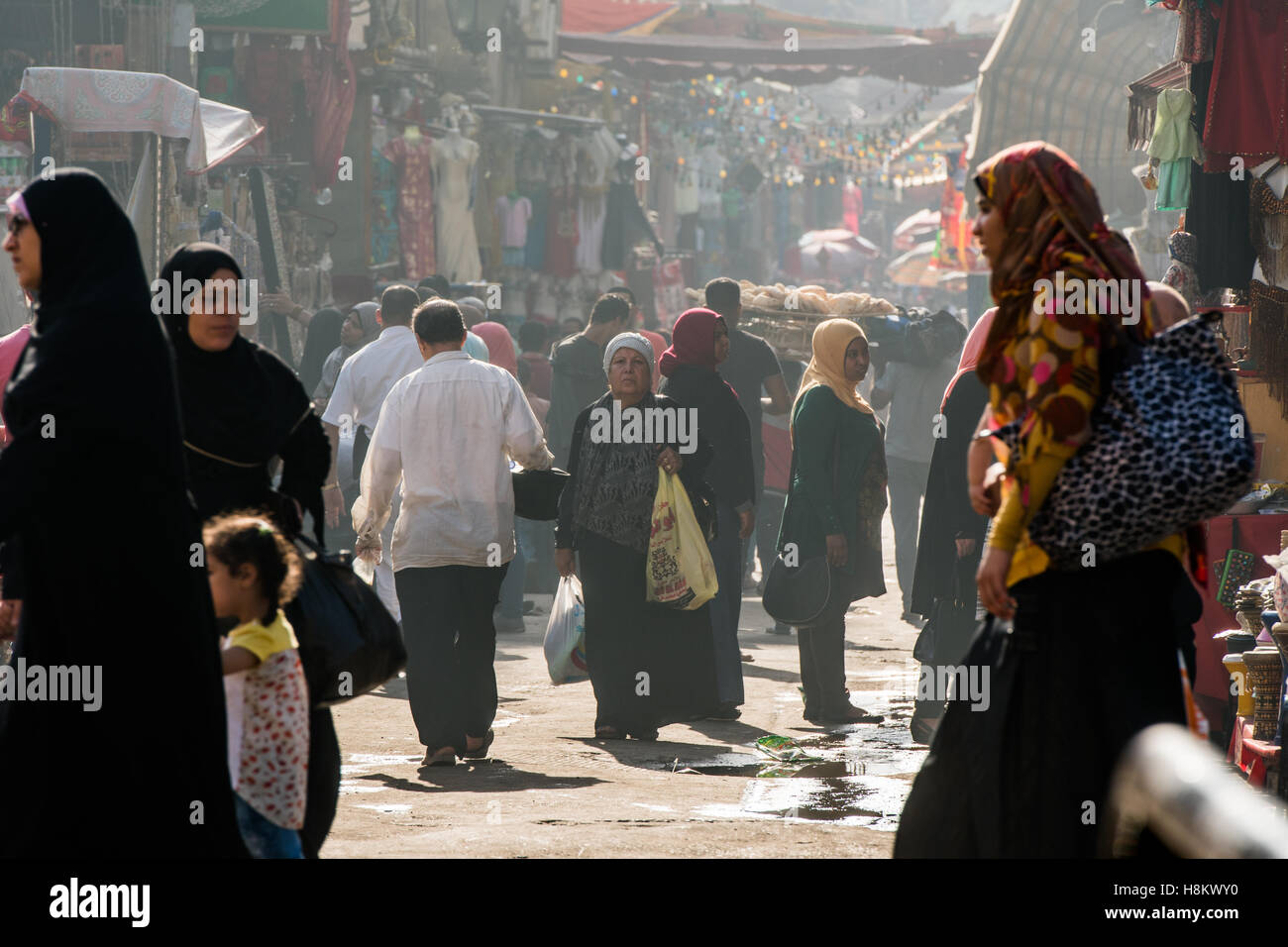 Kairo, Ägypten. Ägyptische Männer und Frauen mit Kopftüchern zu Fuß durch Geschäfte und im Gespräch mit Ladenbesitzer entlang einer Gasse bedeckt Stockfoto