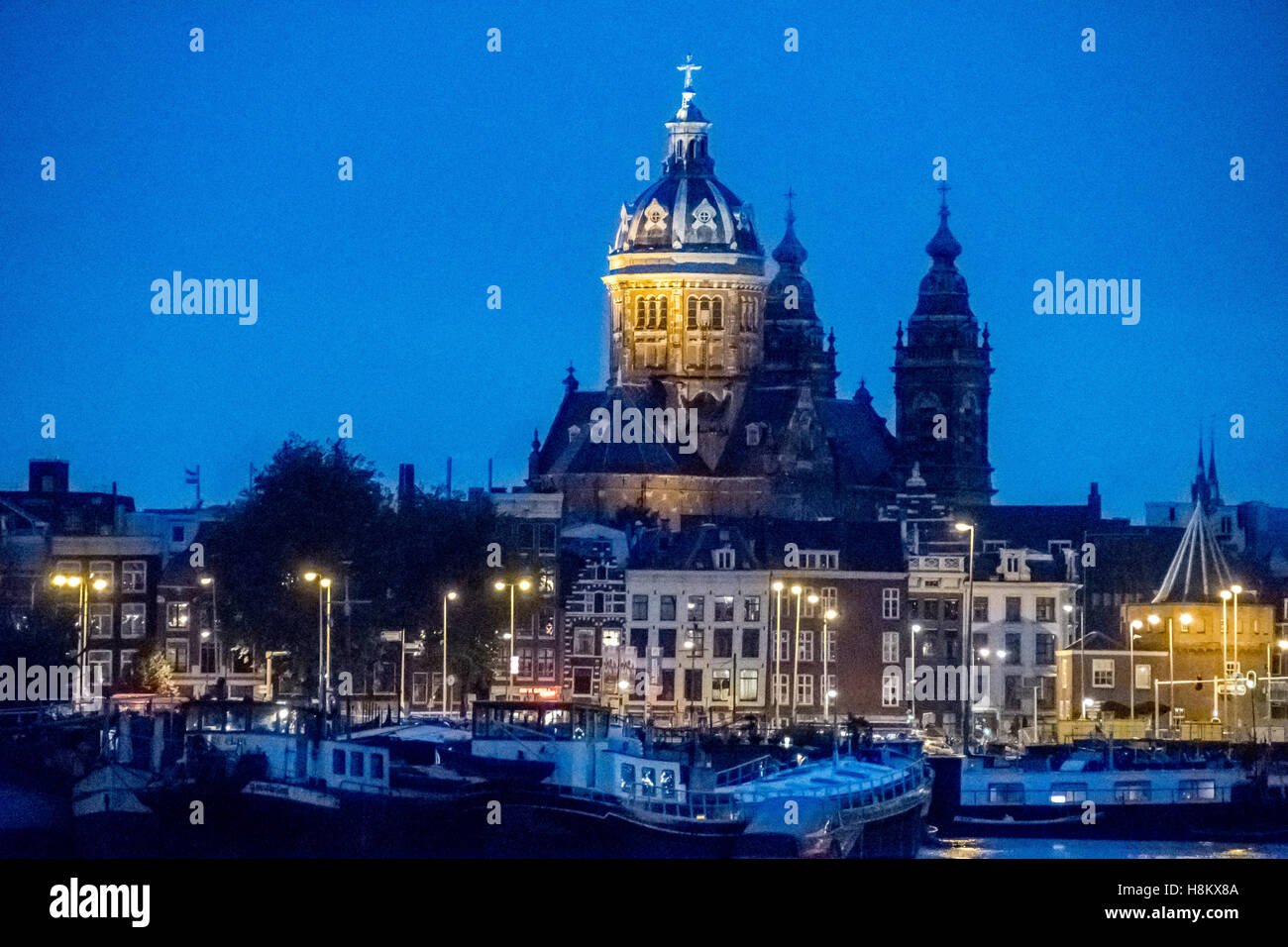 Amsterdam, Niederlande-Boote im Kanal mit Wasser-Ansicht der St. Nikolaus-Kathedrale in der Nacht angedockt. Stockfoto