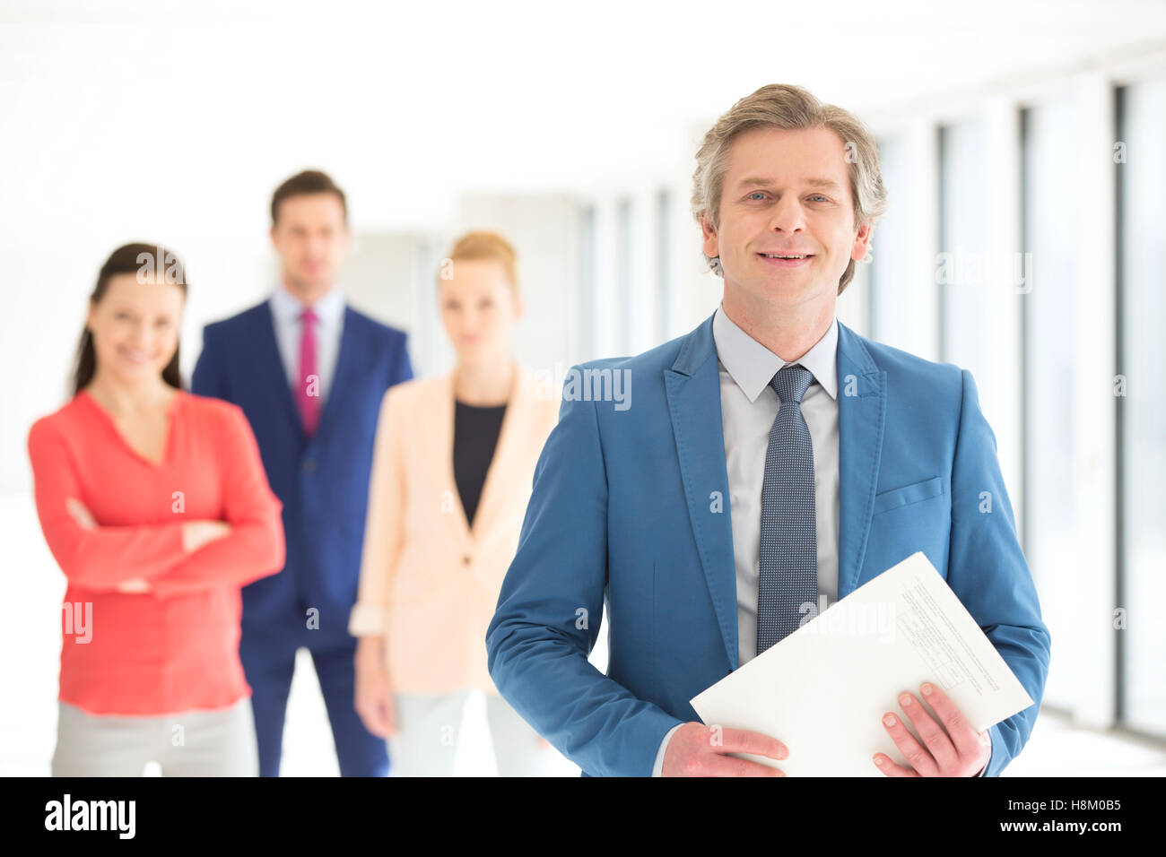 Porträt von zuversichtlich Geschäftsmann hält Dokument mit Team im Hintergrund im Büro Stockfoto