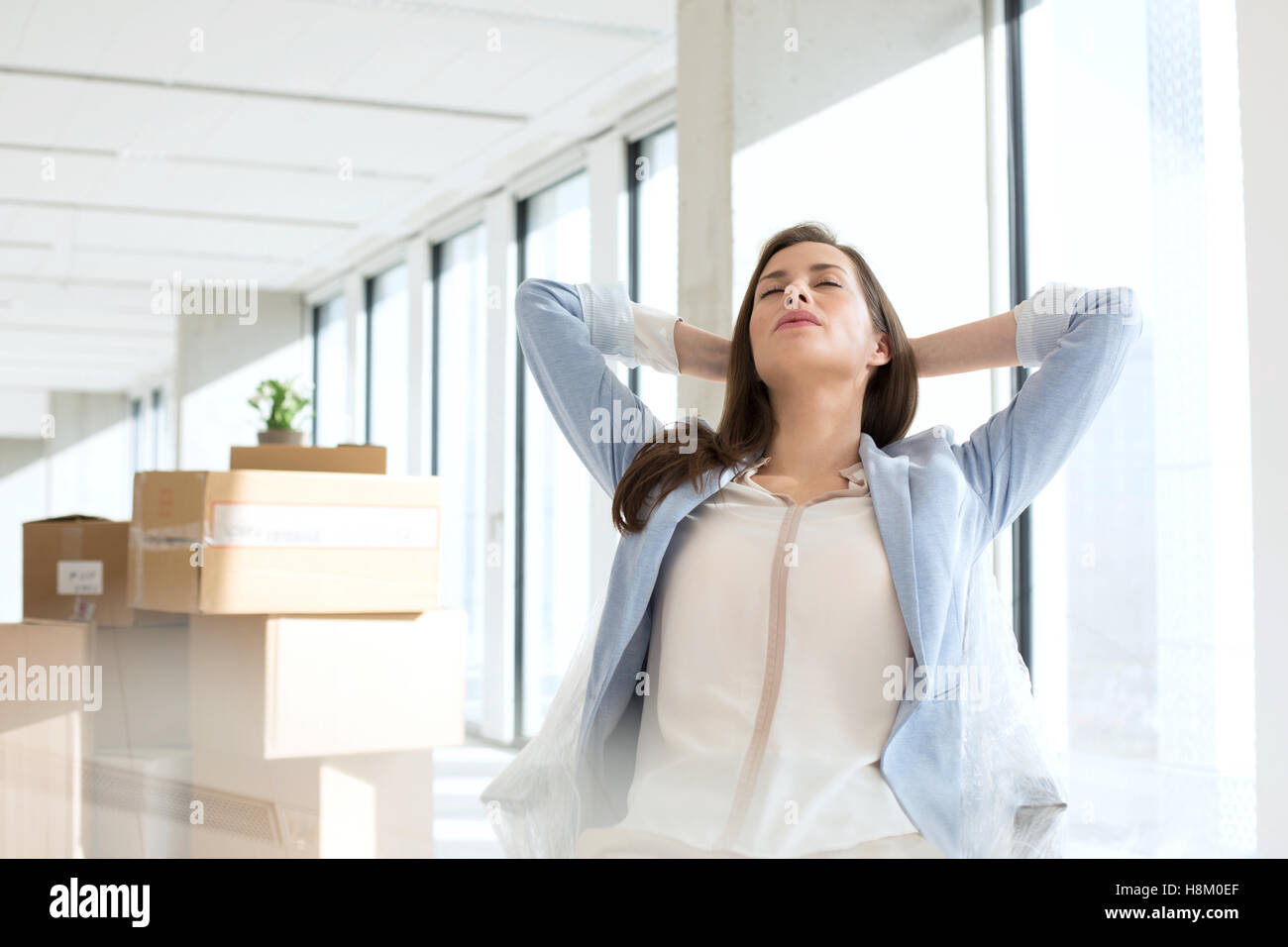 Entspannte junge Geschäftsfrau mit Händen hinter dem Kopf im neuen Büro Stockfoto