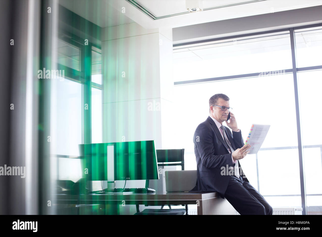 Reife Geschäftsmann halten Dokument beim Telefonieren mit Handy im Büro Stockfoto