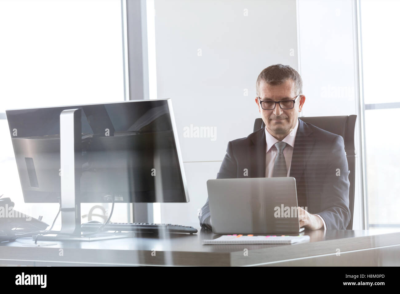 Zuversichtlich reifer Geschäftsmann mit Laptop am Schreibtisch im Büro Stockfoto