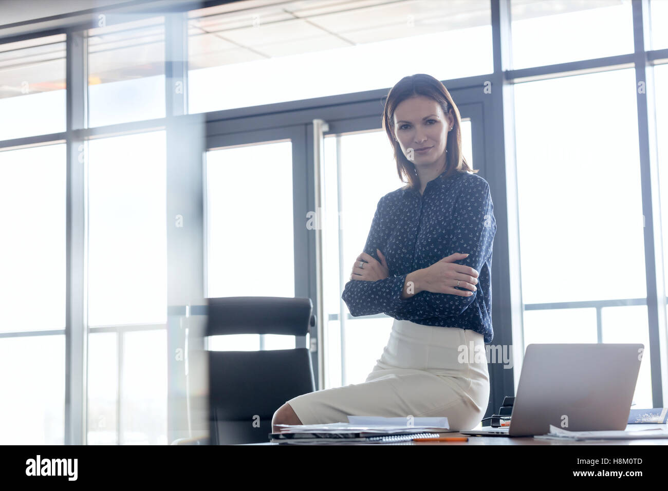 Porträt der jungen Unternehmerin sitzen Arme gekreuzt auf Schreibtisch im Büro Stockfoto