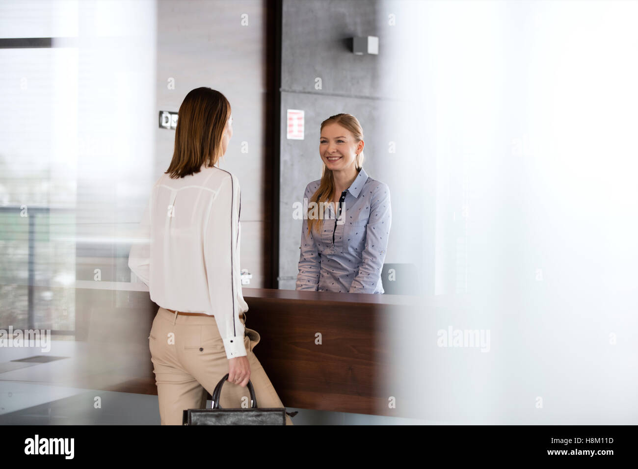 Glückliche junge Empfangsdame im Gespräch mit Geschäftsfrau im Büro Stockfoto