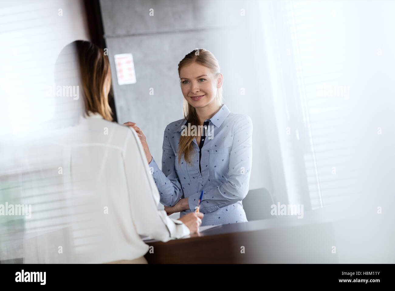 Junge Angestellte an der Rezeption sprechen mit Geschäftsfrau im Büro Stockfoto