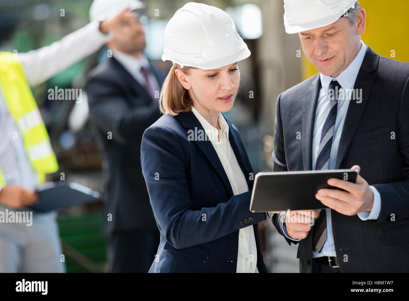 Unternehmer und Unternehmerin mit digital-Tablette mit Kollegen im Hintergrund bei industry Stockfoto