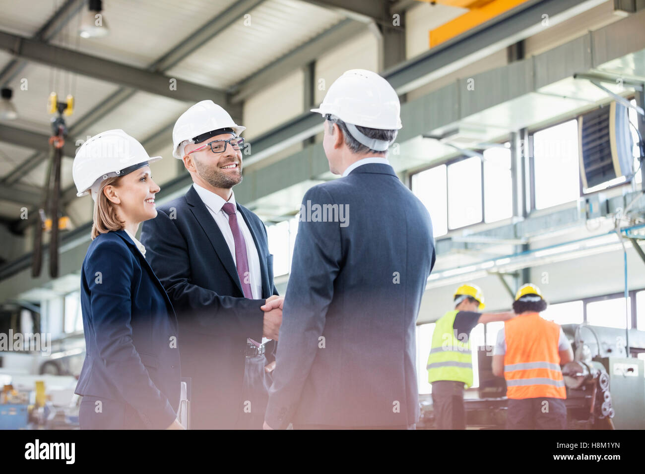 Geschäftsleute Händeschütteln mit Arbeitnehmer, die im Hintergrund in der Metallindustrie Stockfoto