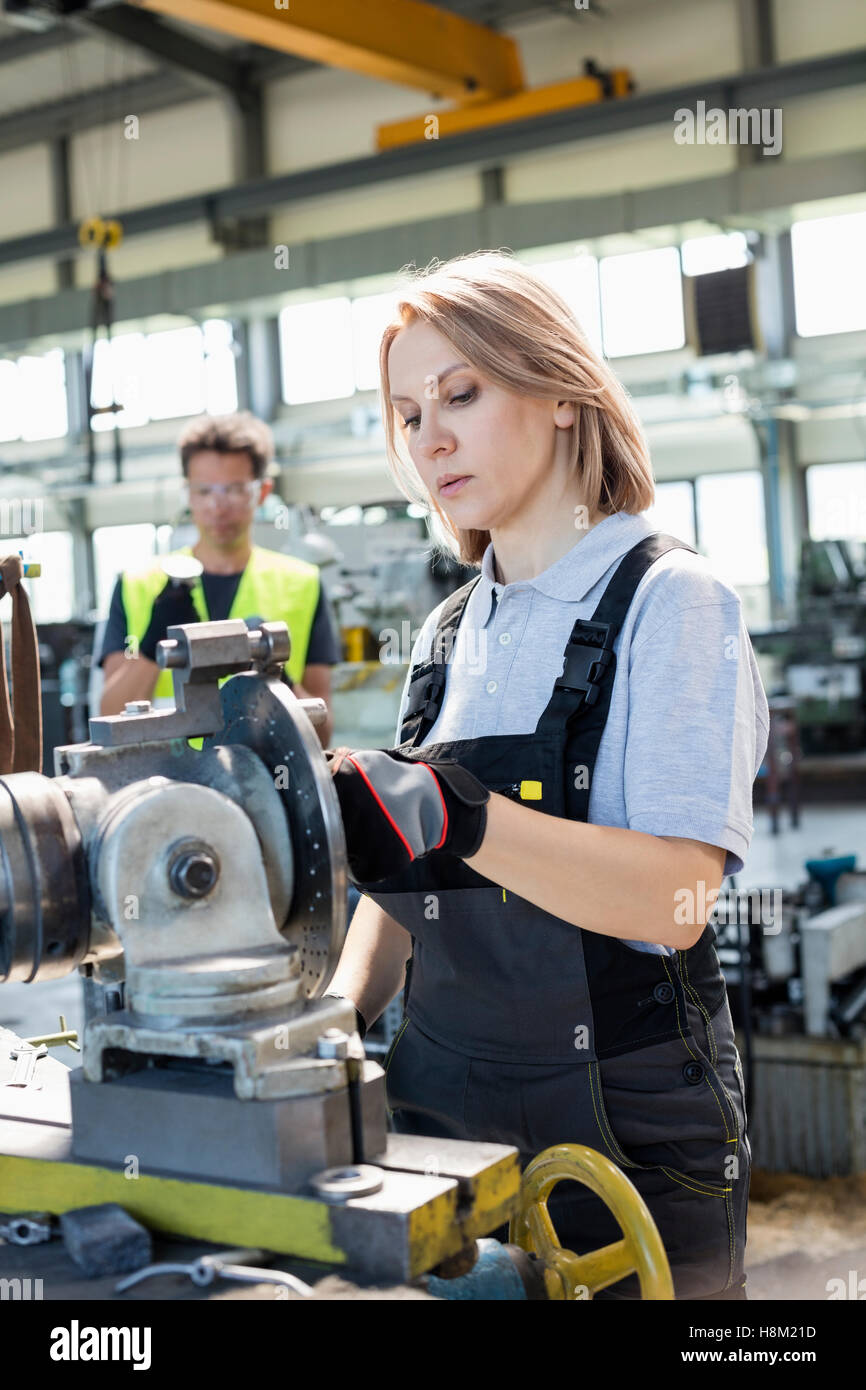 Ältere Arbeitnehmerin arbeiten an Maschinen mit Kollegen im Hintergrund im Werk Stockfoto