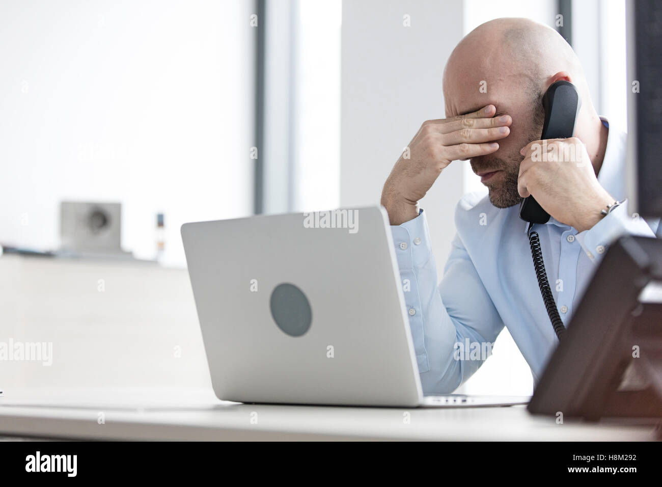 Mitte adult Geschäftsmann mit Telefon am Schreibtisch im Büro müde Stockfoto