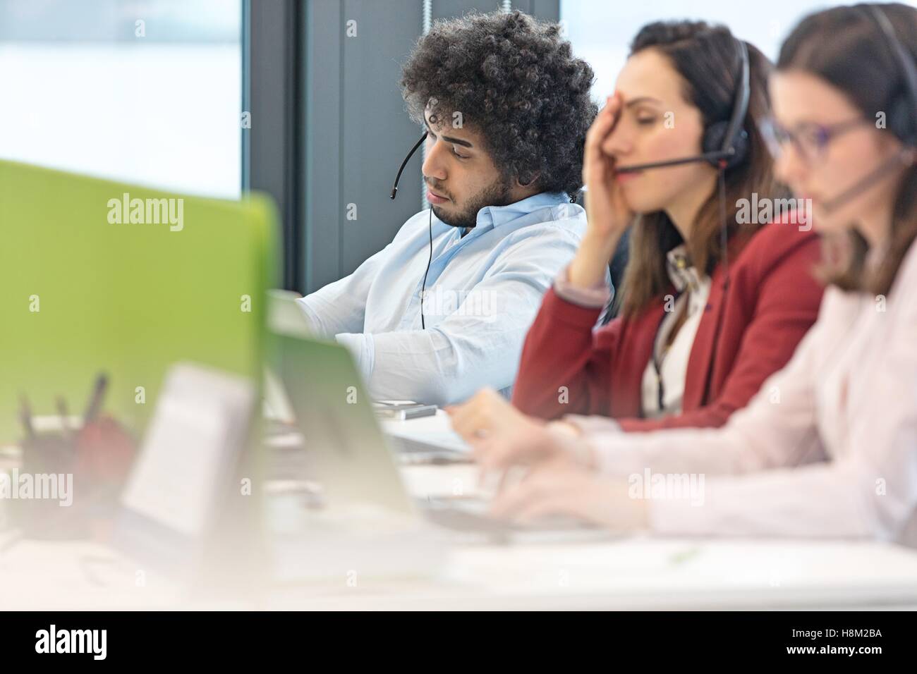 Müden männlichen Mitarbeiter des Kundendienstes mit Kollegen im Büro arbeiten Stockfoto