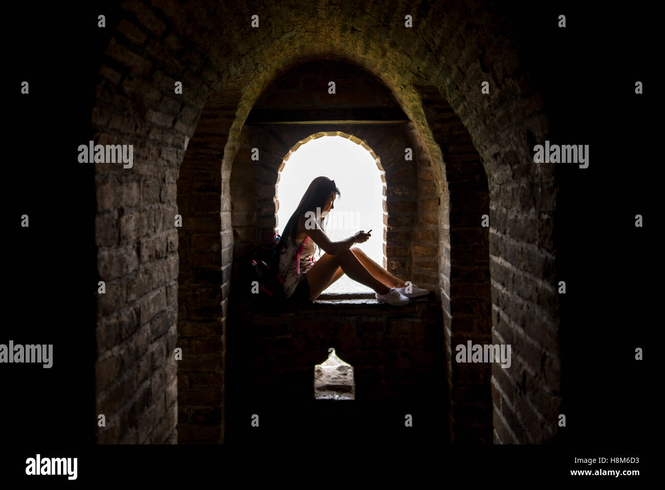 Mutianyu, China - Silhouette einer jungen chinesischen Frau auf ihrem Handy auf ein Fenster innerhalb der chinesischen Mauer sitzen. Die Stockfoto