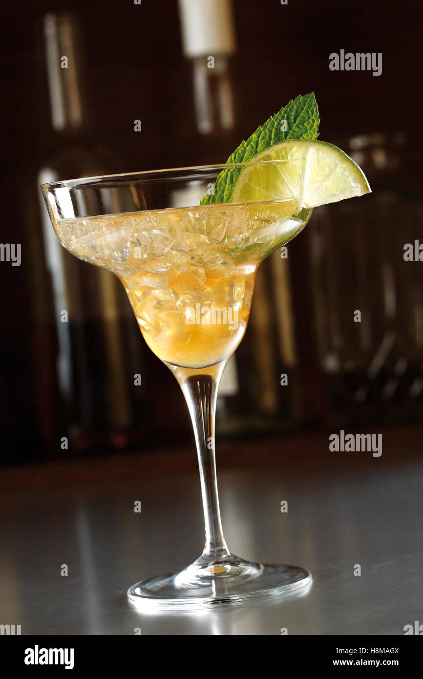 Erfrischenden cocktail in ein hohes Glas auf den Tresen einer Bar in dunklen Ambiente. Mit Limette und Minze dekoriert. Stockfoto