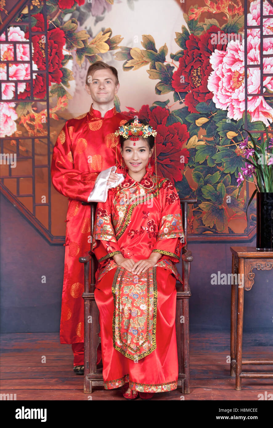 Gemischte Rennen Braut und Bräutigam in Studio tragen traditionelle chinesische Hochzeit outfits Stockfoto