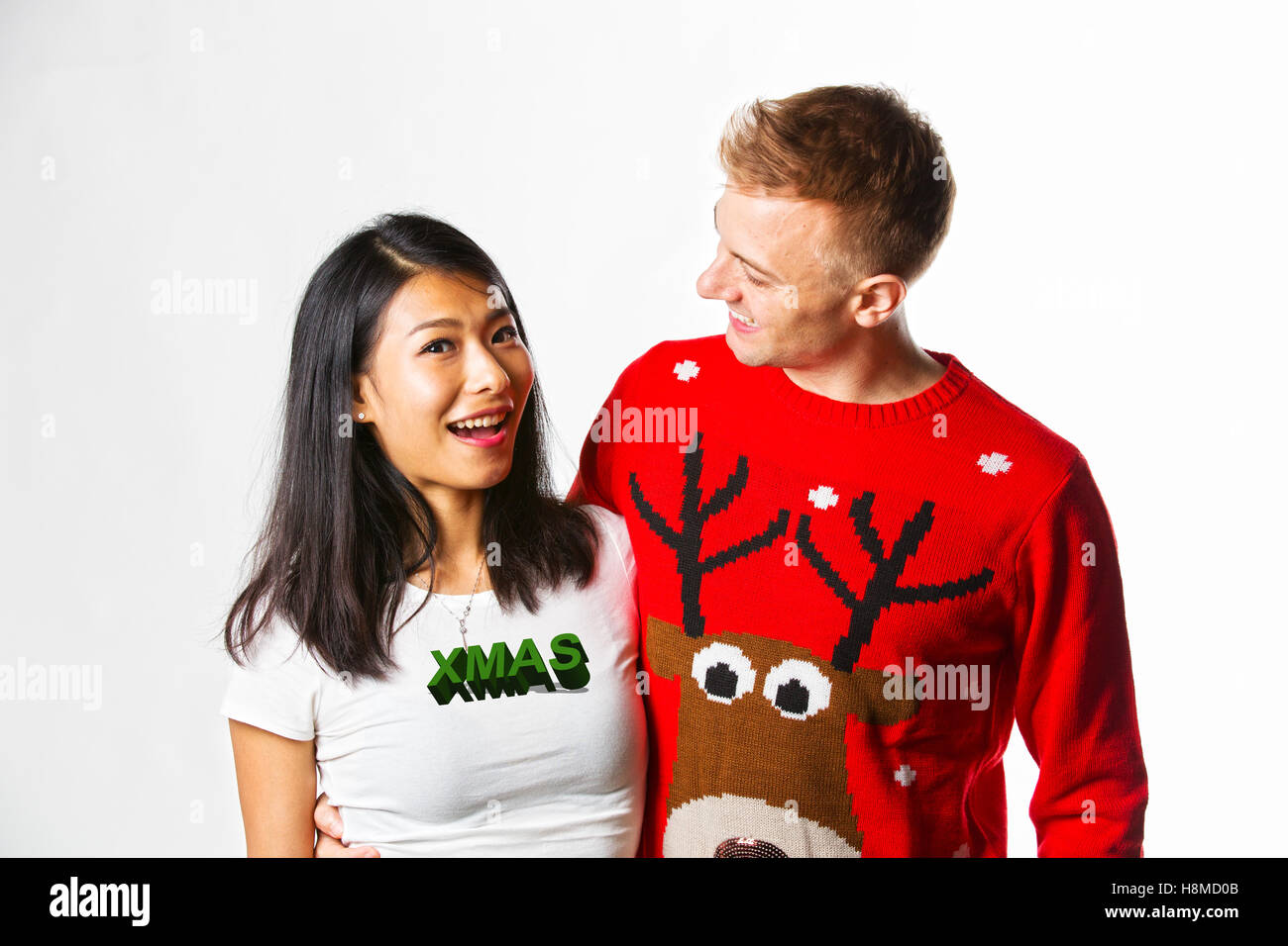 Porträt von glücklich Multi ethnischen paar Weihnachten Jumper im Studio tragen, während sich gegenseitig auf der Suche Stockfoto