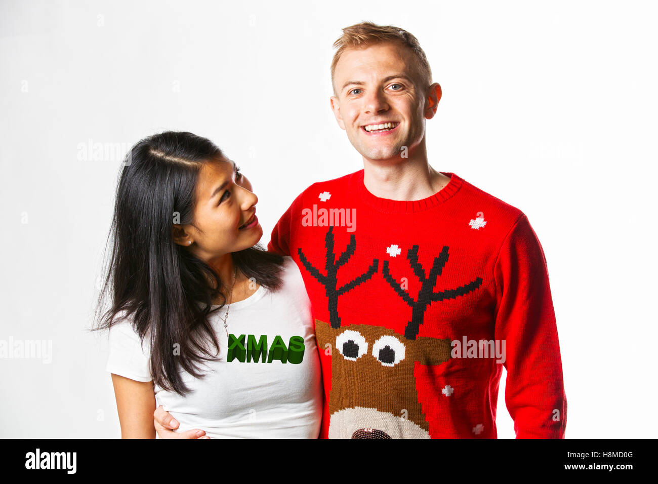 Porträt von glücklich Multi ethnischen paar Weihnachten Jumper im Studio tragen, während sich gegenseitig auf der Suche Stockfoto