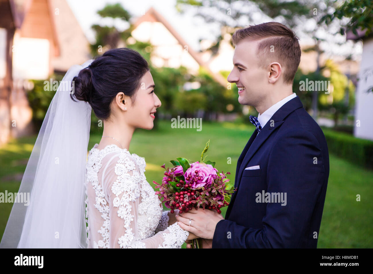 Seitenansicht des Lächelns Hochzeitspaar halten Blumenstrauß auf dem lawn Stockfoto
