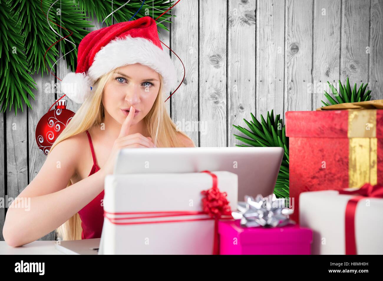 Frau mit Finger auf Lippe mit Laptop neben Weihnachtsgeschenk Stockfoto
