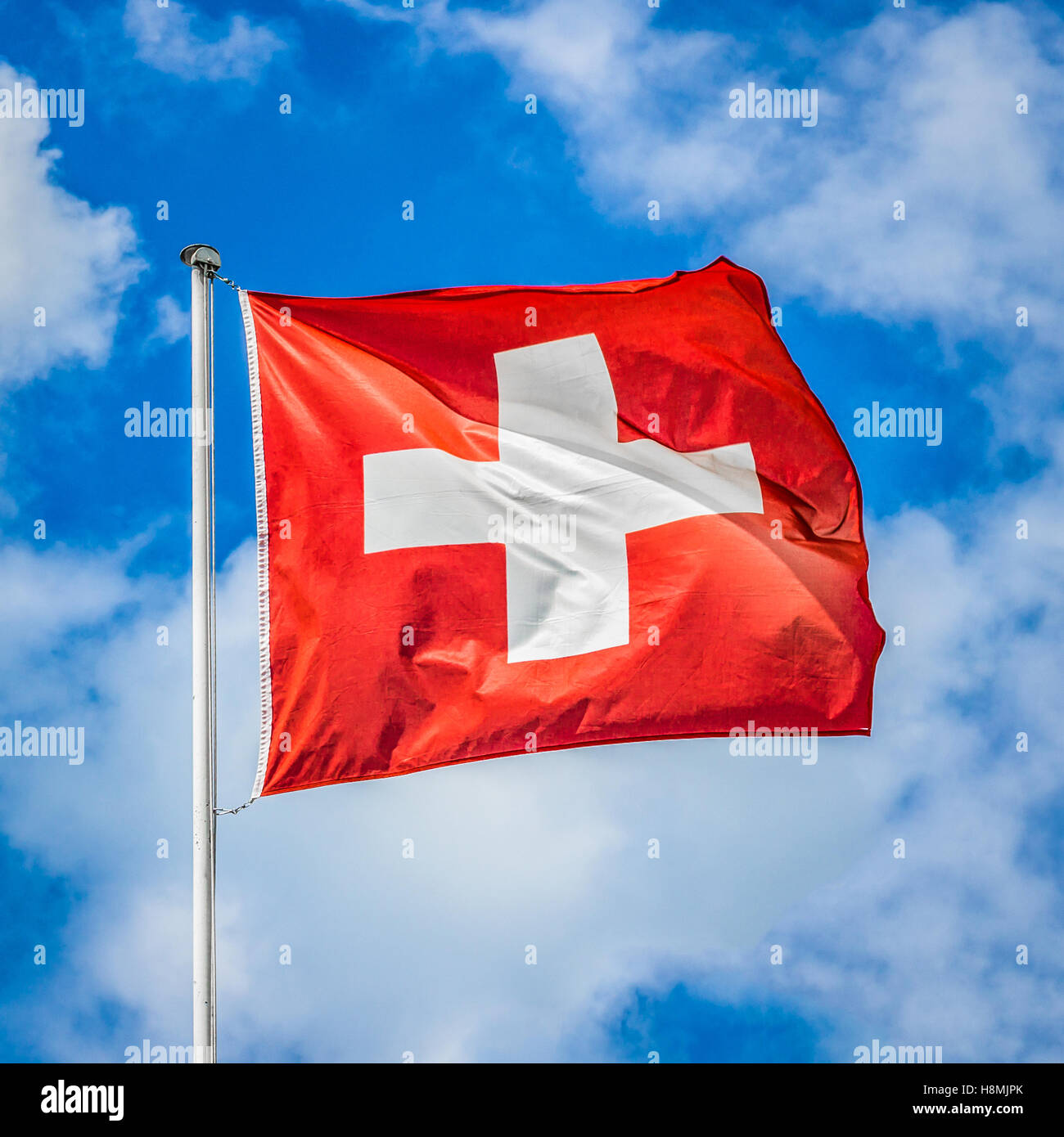 Klassische Ansicht der Nationalflagge der Schweiz winken im Wind vor blauem Himmel mit Wolken an einem sonnigen Tag Stockfoto
