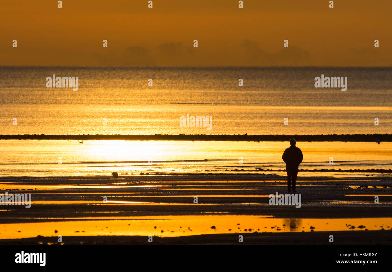 Person, die allein am Strand bei Sonnenuntergang. Stockfoto