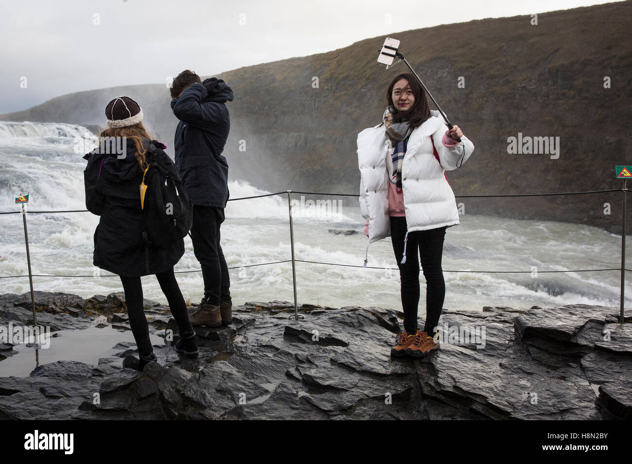 Eine Frau nimmt ein Selbstporträt mit einem Selfie-Stick am Gullfoss Wasserfall in Island Stockfoto