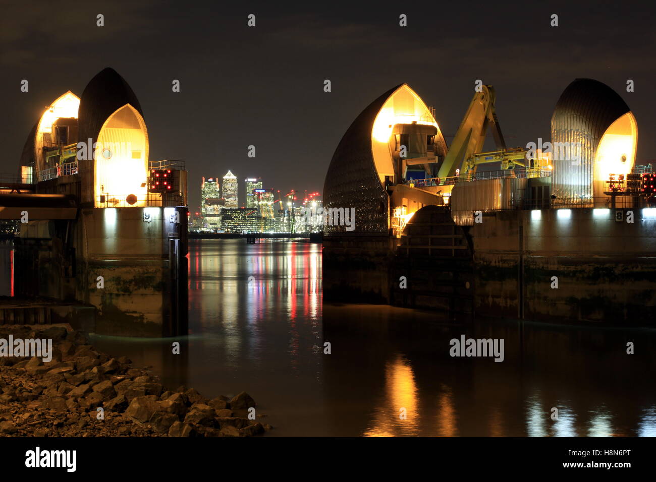 Die Thames Barrier in der Nacht mit den Lichtern des Canary Wharf im fernen Hintergrund. Stockfoto