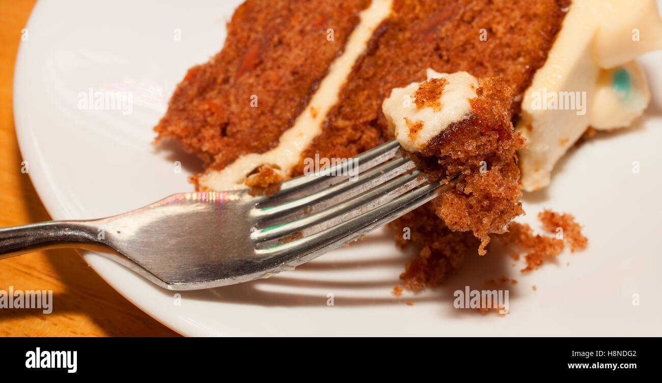 Karotte-Kuchen auf einer Gabel mit mehr auf einem weißen Teller hinter Stockfoto