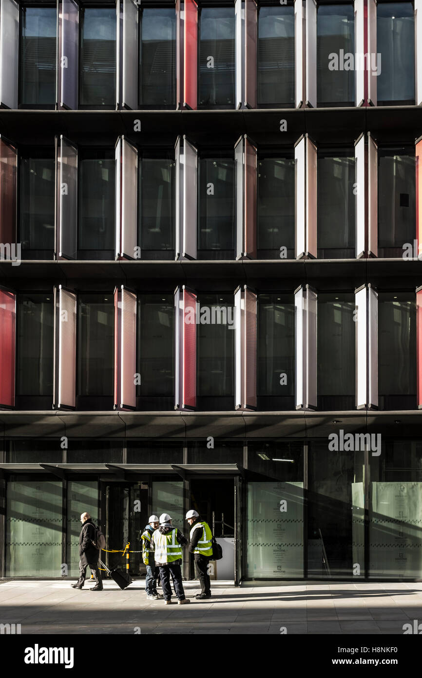 Mitarbeiter in gelb 'Hi-viz' Jacken und weißen Helmen stehen vor einem Mizuho House in London. Stockfoto
