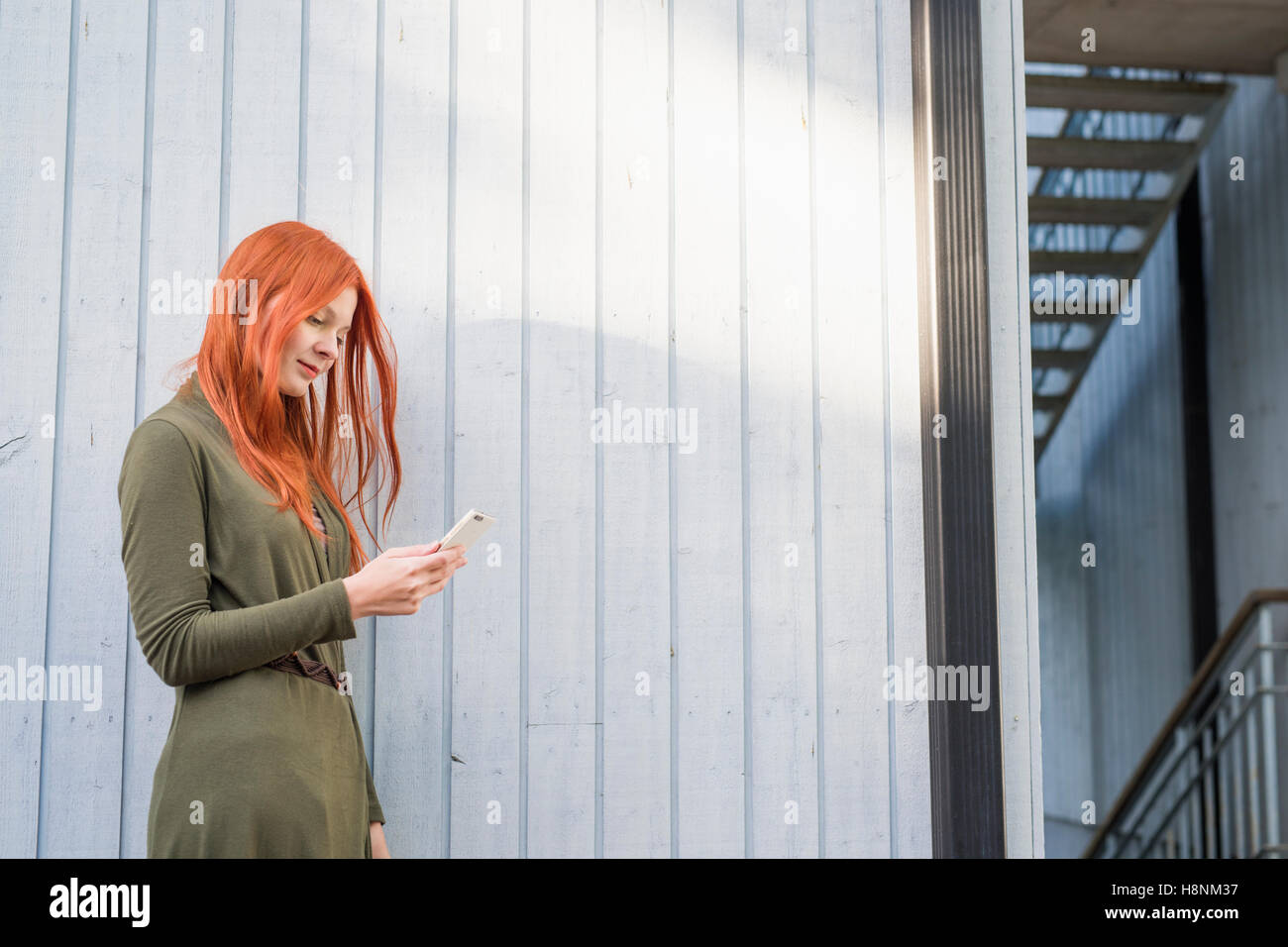 Rothaarige Frau mit Telefon gegen weiße Wand Stockfoto