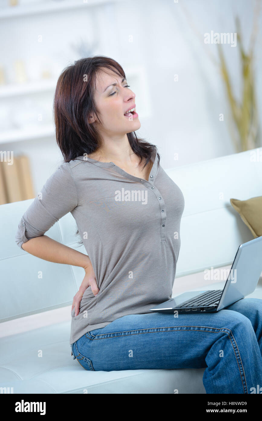 junge Frau sitzt auf dem Sofa, die unter Rückenschmerzen leiden Stockfoto