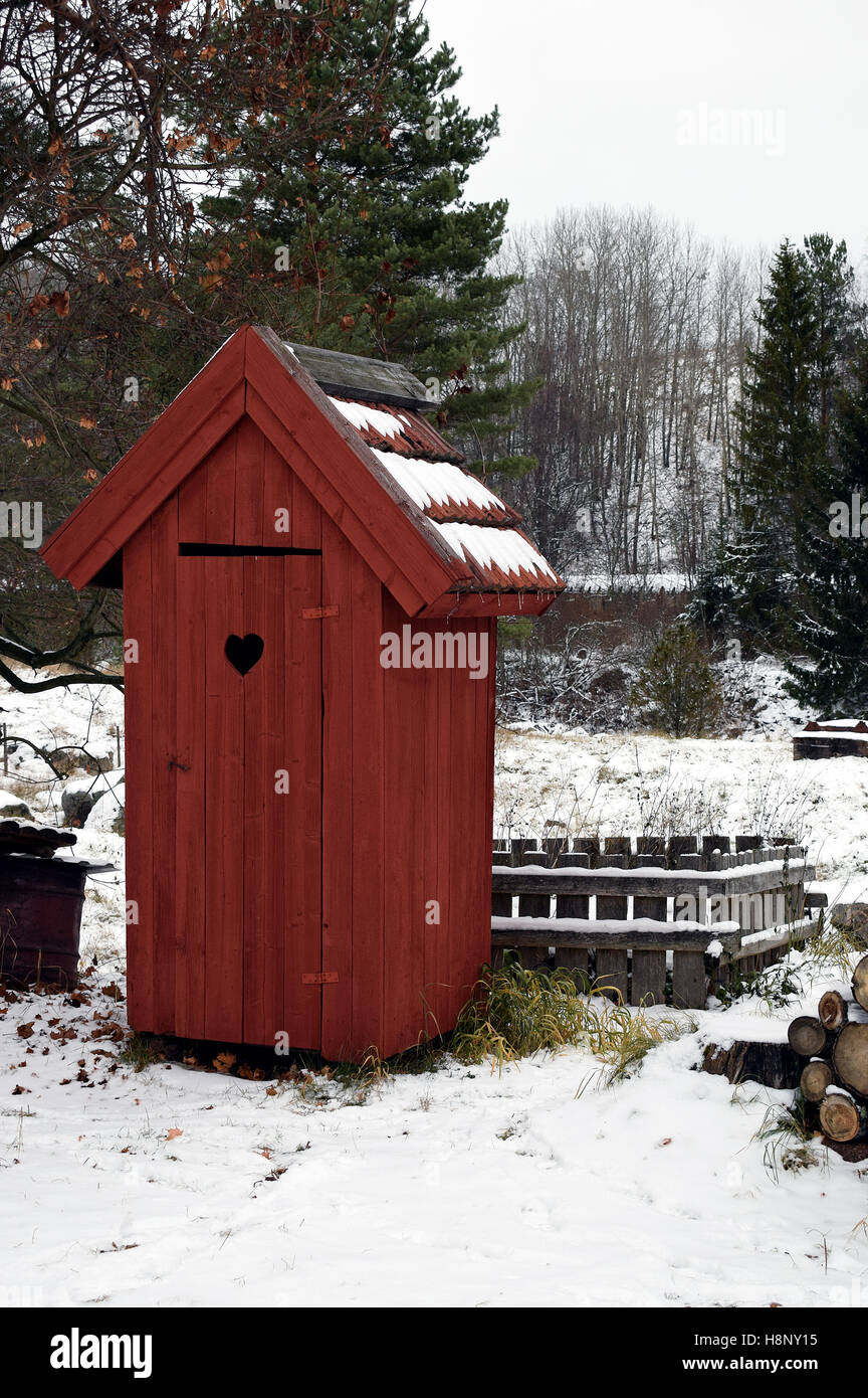 Rotes hölzernes Plumpsklo WC im Winter. Stockfoto