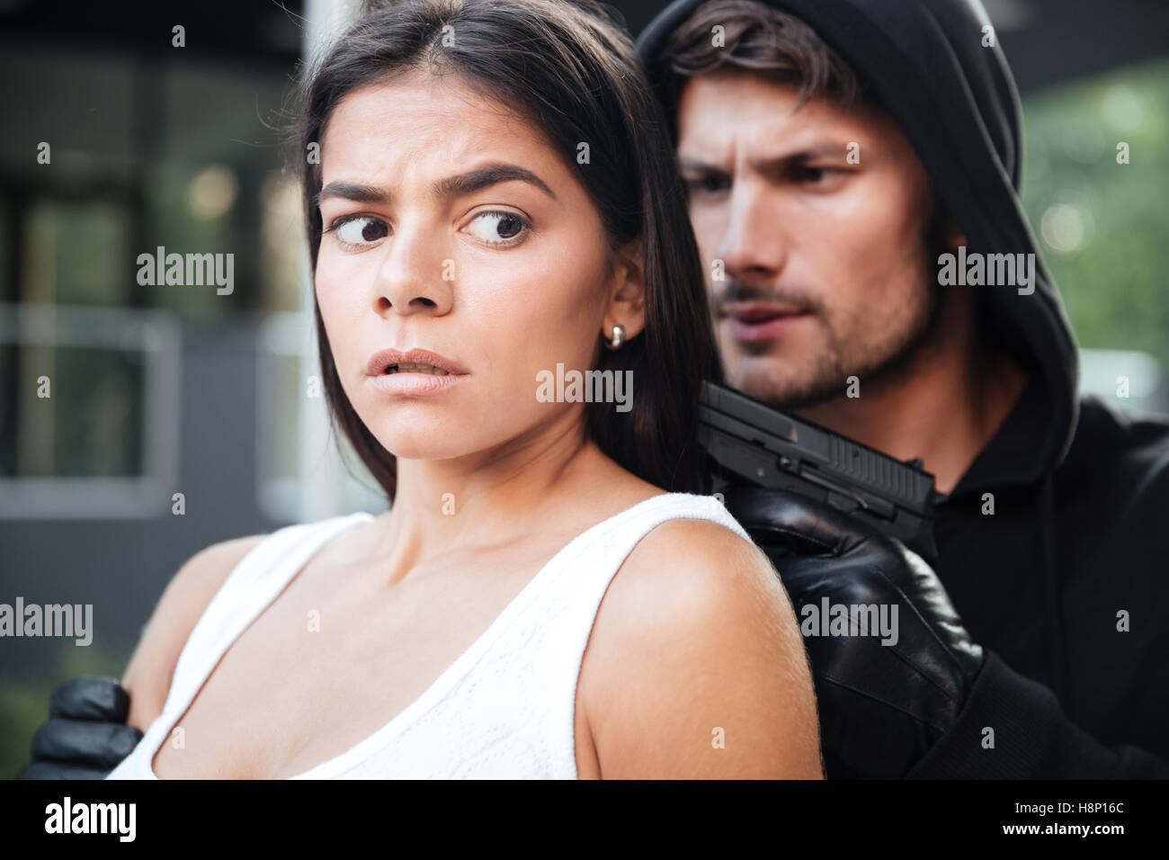 Mann-Räuber in Hoodie drohte mit Pistole, verängstigte junge Frau im freien Stockfoto