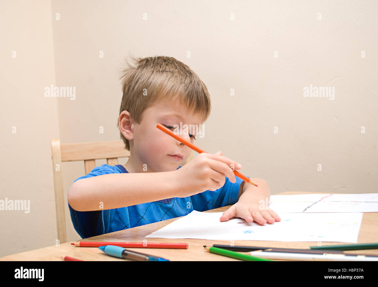 Ein kleiner Kindergarten junge konzentriert sich, wie er am Tisch im Haus Familie zieht. Stockfoto