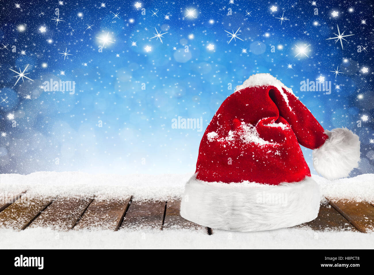 Weihnachten Xmas Hintergrund mit Weihnachtsmann Mütze Kappe auf verschneiten Holzbohlen vor blaue Nacht Himmel, Sterne und Schneeflocken Stockfoto