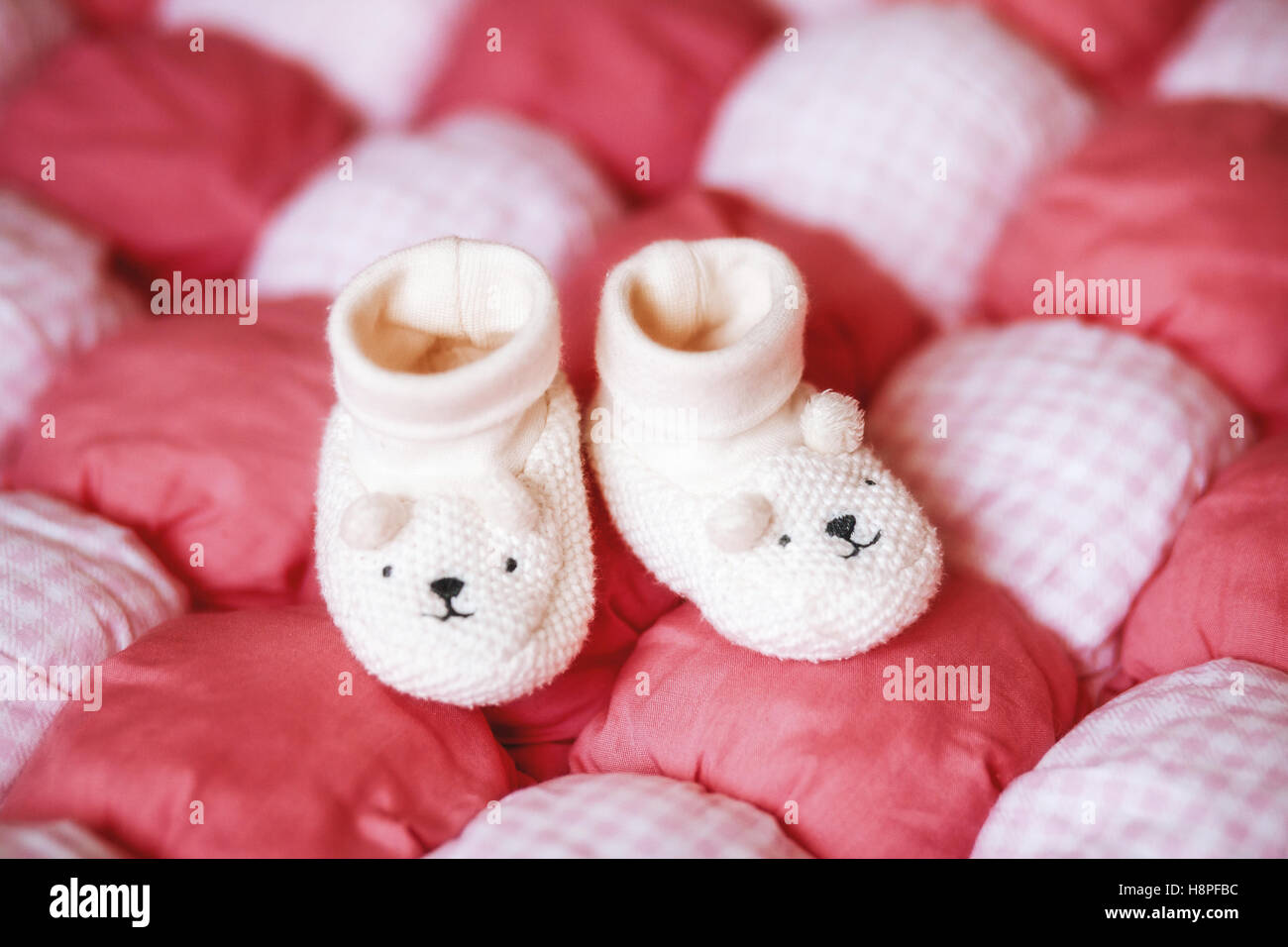 Süße weiße Babyschuhe auf roter Decke. Schwangerschaft-Konzept Stockfoto
