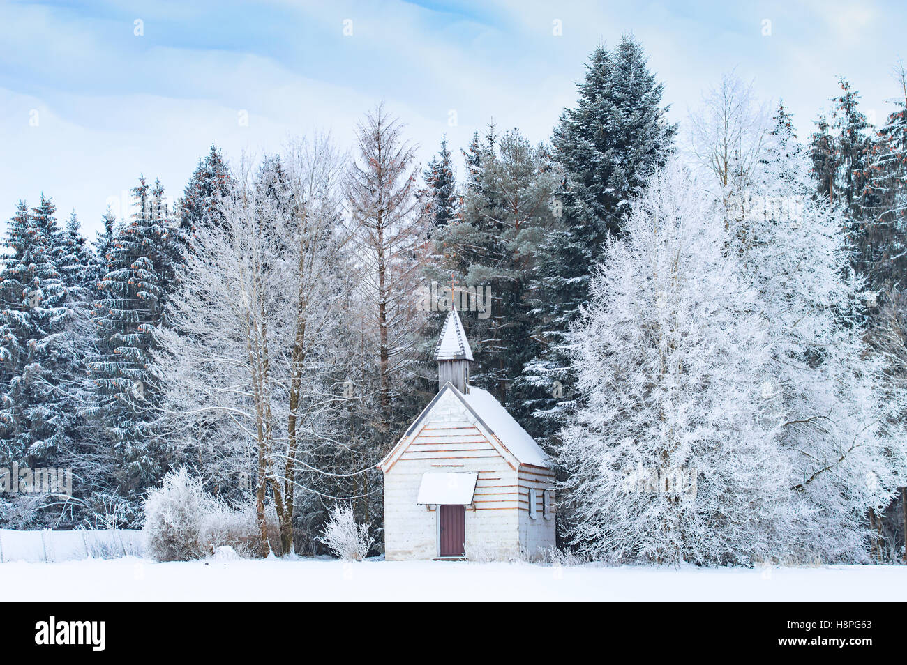 Kleine Holzkapelle auf verschneiten frostigen Waldwiese im verschneiten gefrorenen Wald. Wunderbare Winterlandschaft im Bayerischen Raum Allgäu Stockfoto