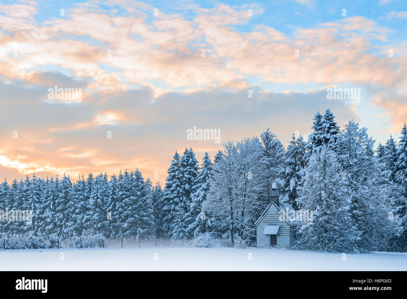 Kleine Holzkapelle in verschneiten frostigen Wald unter Sonnenaufgang Morgenhimmel. Erstaunliche idyllische Winterlandschaft Stockfoto