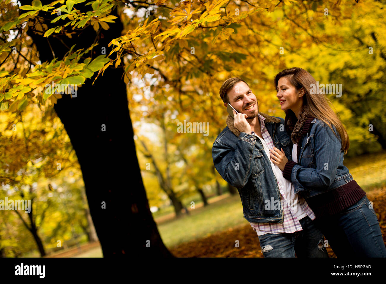 Junges Liebespaar im herbstlichen Park und Mann am Telefon sprechen Stockfoto