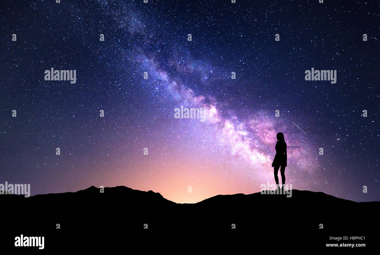 Schöne lila Milchstraße mit Frau. Bunte Landschaft mit Nachthimmel mit Sternen und Silhouette eines Mädchens Stockfoto