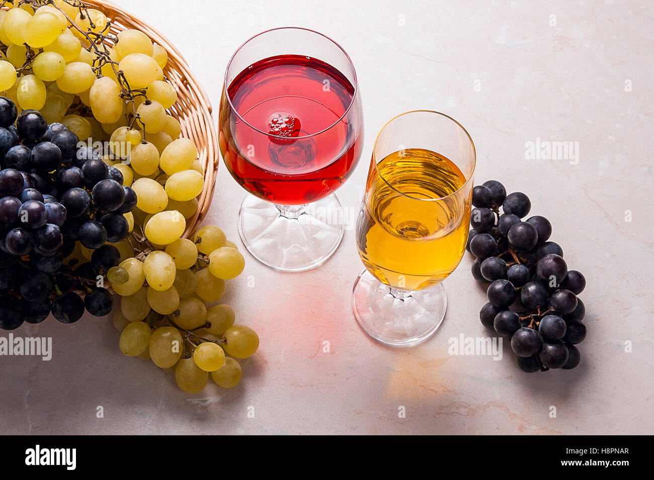 Zwei Gläser - mit Weißwein und Rotwein auf hellem Marmor Hintergrund. Trauben von grünen und roten Trauben Stockfoto