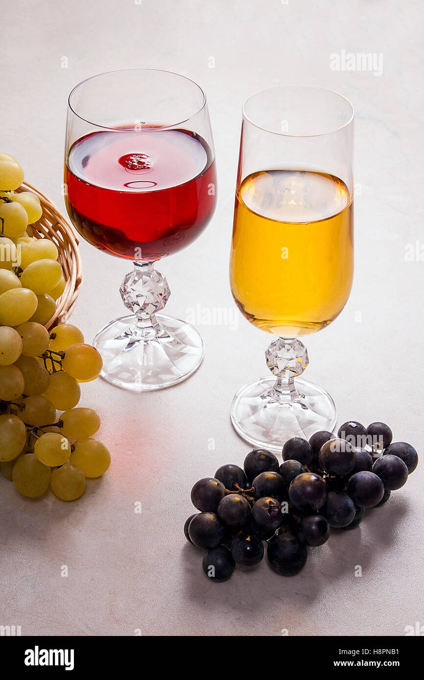 Zwei Gläser - mit Weißwein und Rotwein auf hellem Marmor Hintergrund. Trauben von grünen und roten Trauben Stockfoto