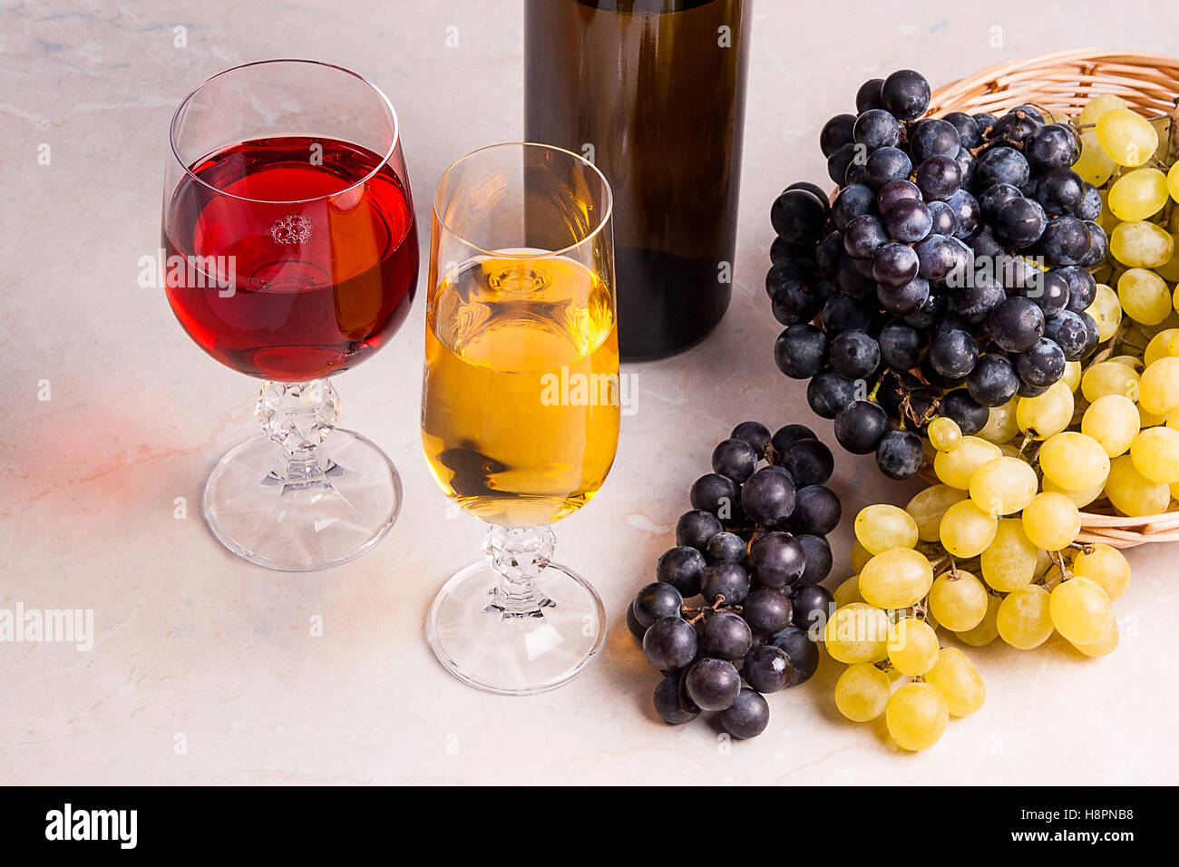 Zwei Gläser - eine mit Weißwein und eine mit roten Wein und braune Flasche mit Weißwein auf hellen Marmor Hintergrund. Stockfoto