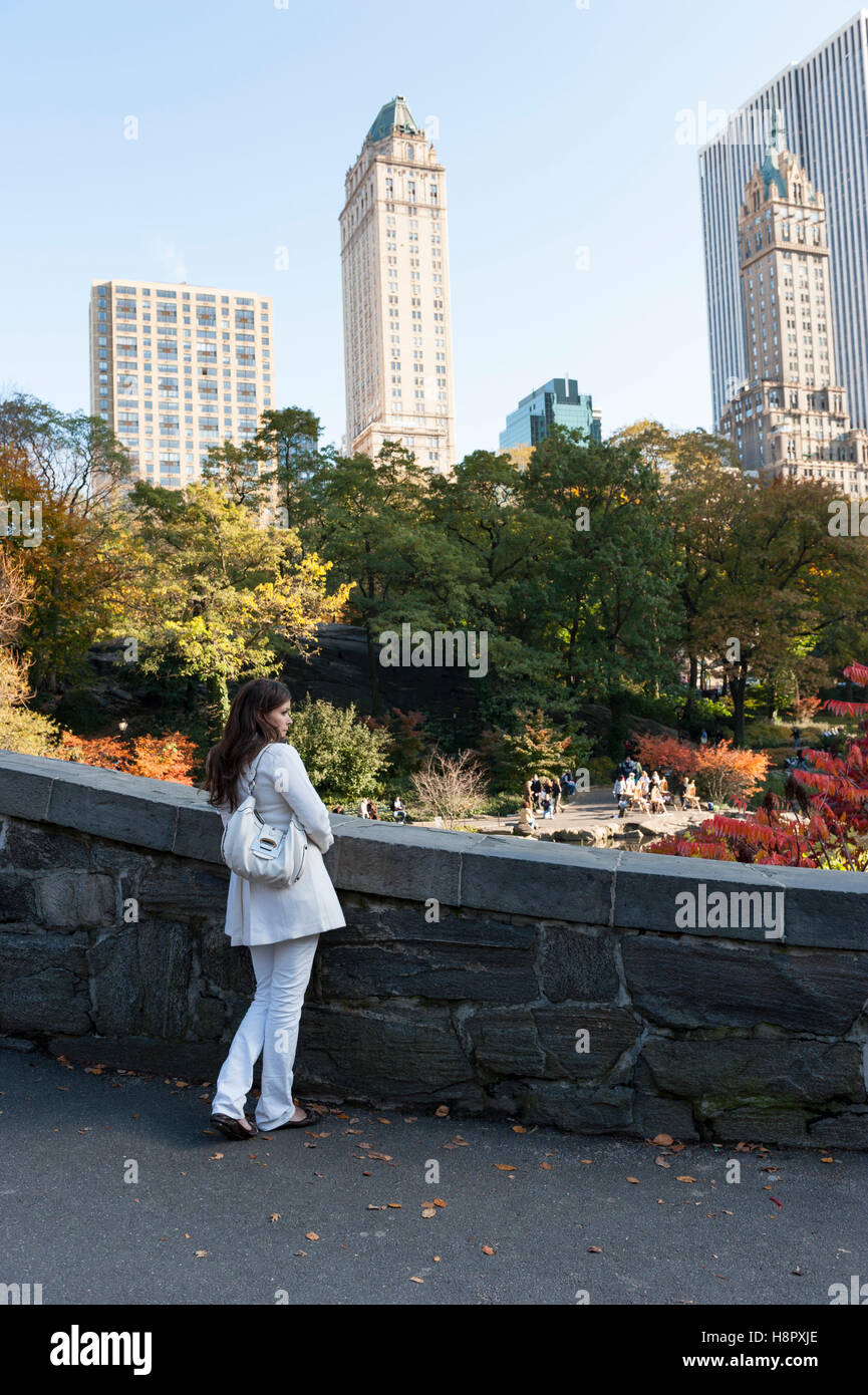 Elegante Reise, Stadtpark, alleinstehende weiße Frau in weißem Outfit, die die Skyline von New York City von einer Brücke im Central Park aus bewundert. Stockfoto