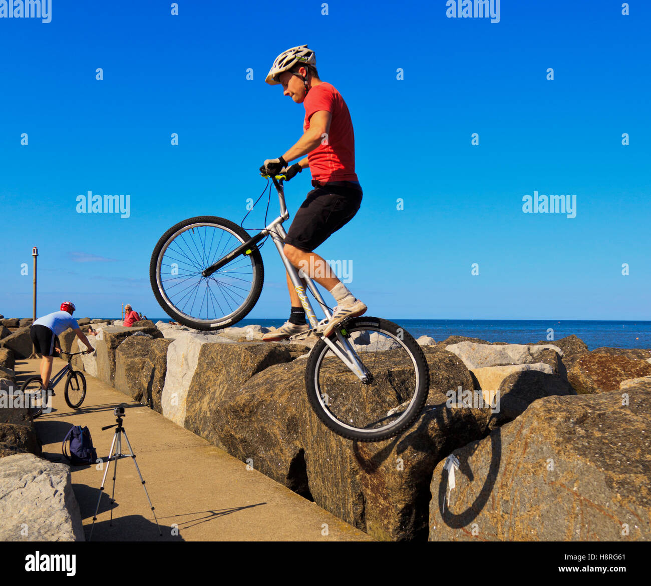 Mountainbiker, springen über Felsen auf der Hafenmauer in Staithes, North Yorkshire Stockfoto