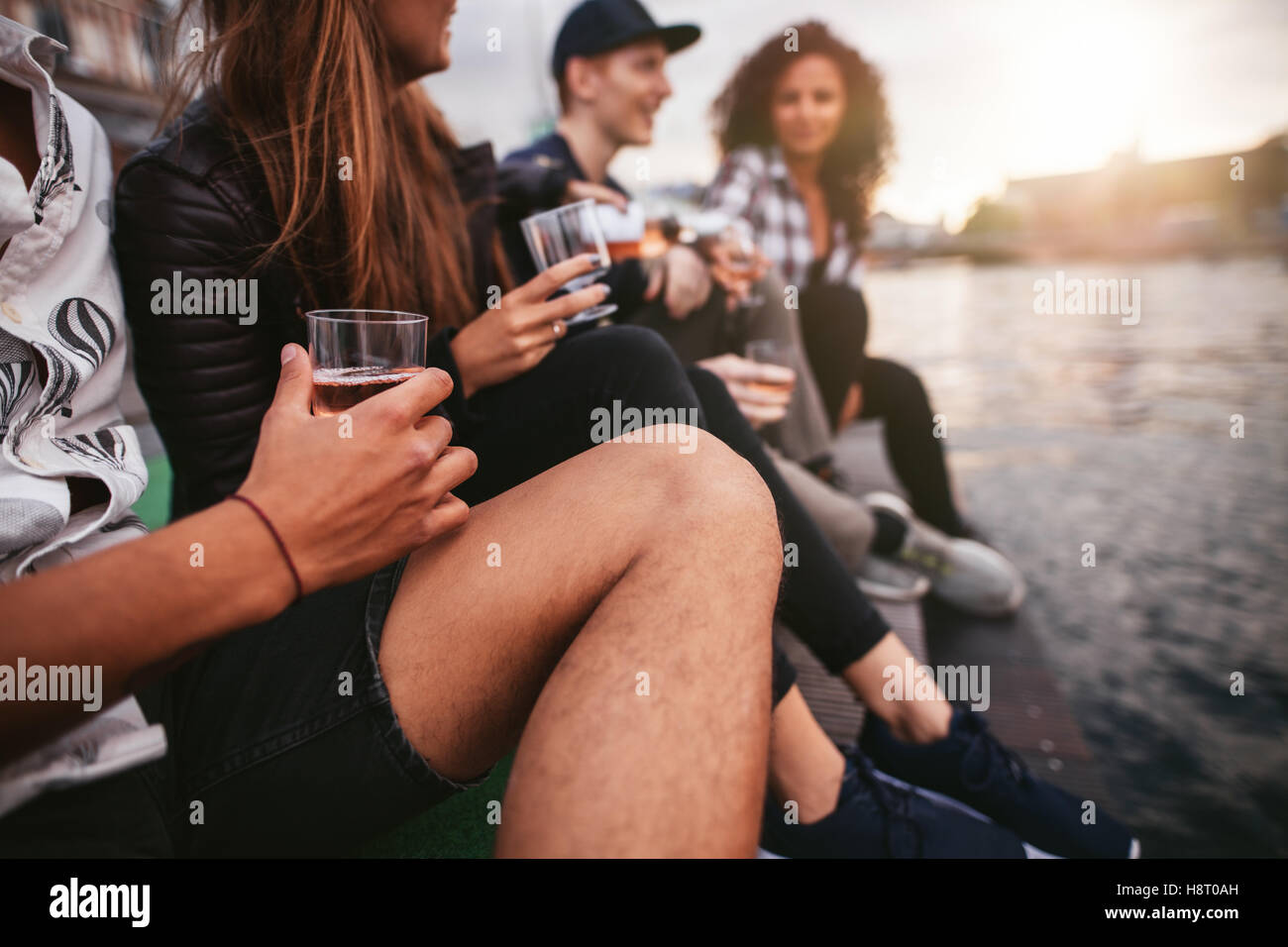 Schuss Gruppe von Menschen sitzen auf Pier und Getränke beschnitten. Freunden rumhängen auf Steg, mit Fokus auf Hände mit Getränken Stockfoto